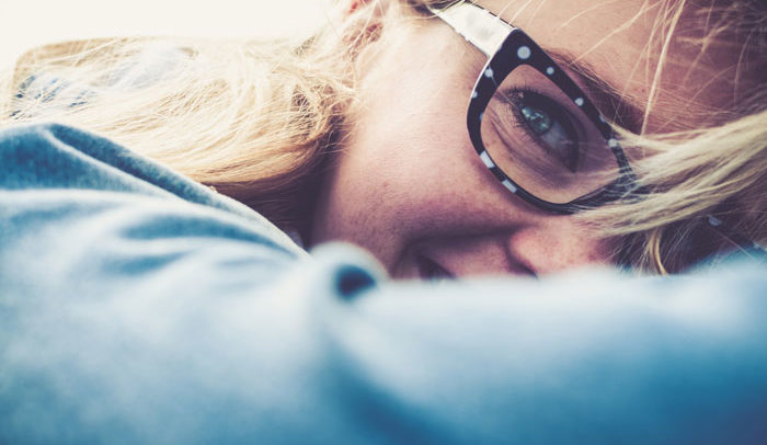young blonde woman playfully smiling and hiding half of her face wearing fun eyeglasses