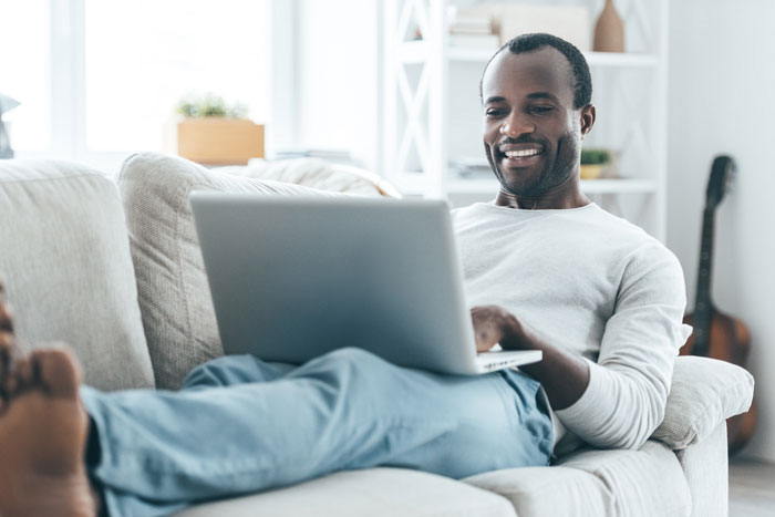 african american man relaxed and happy at home on couch with laptop
