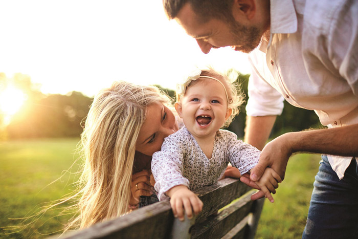 family outside in sunshine on a park bench with smiling baby