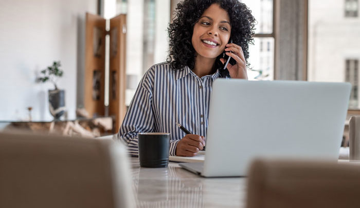 Smiling female entrepreneur sitting at home talking on her cellphone